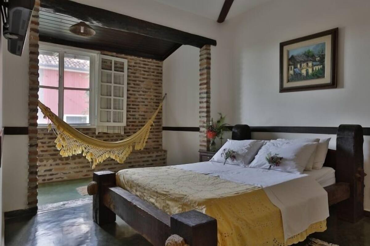 A bedroom with a bed, a hammock, a window, and a painting on the wall.