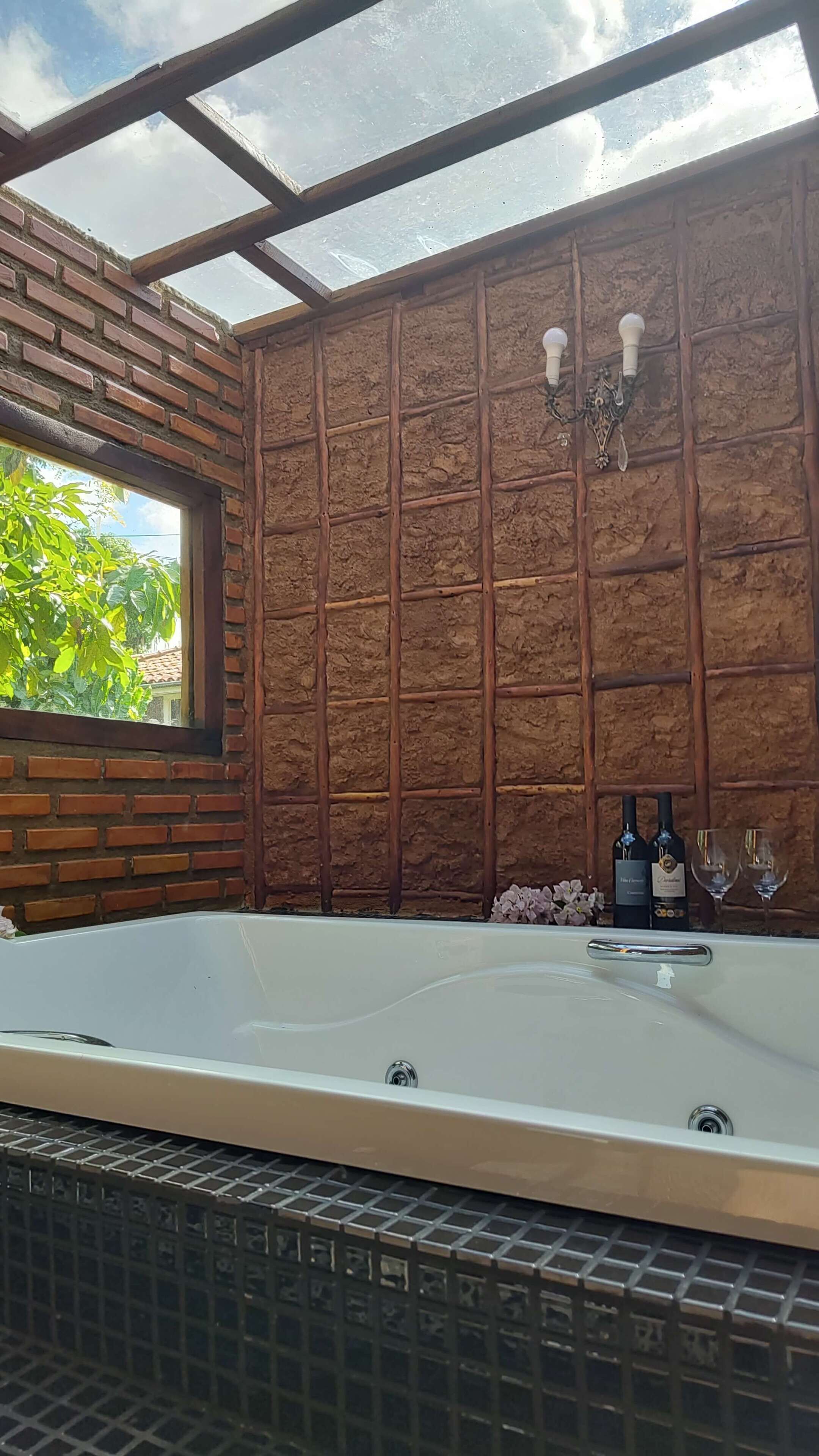 Un baño con una bañera grande, una ventana con vistas a la vegetación y una pared de ladrillo.