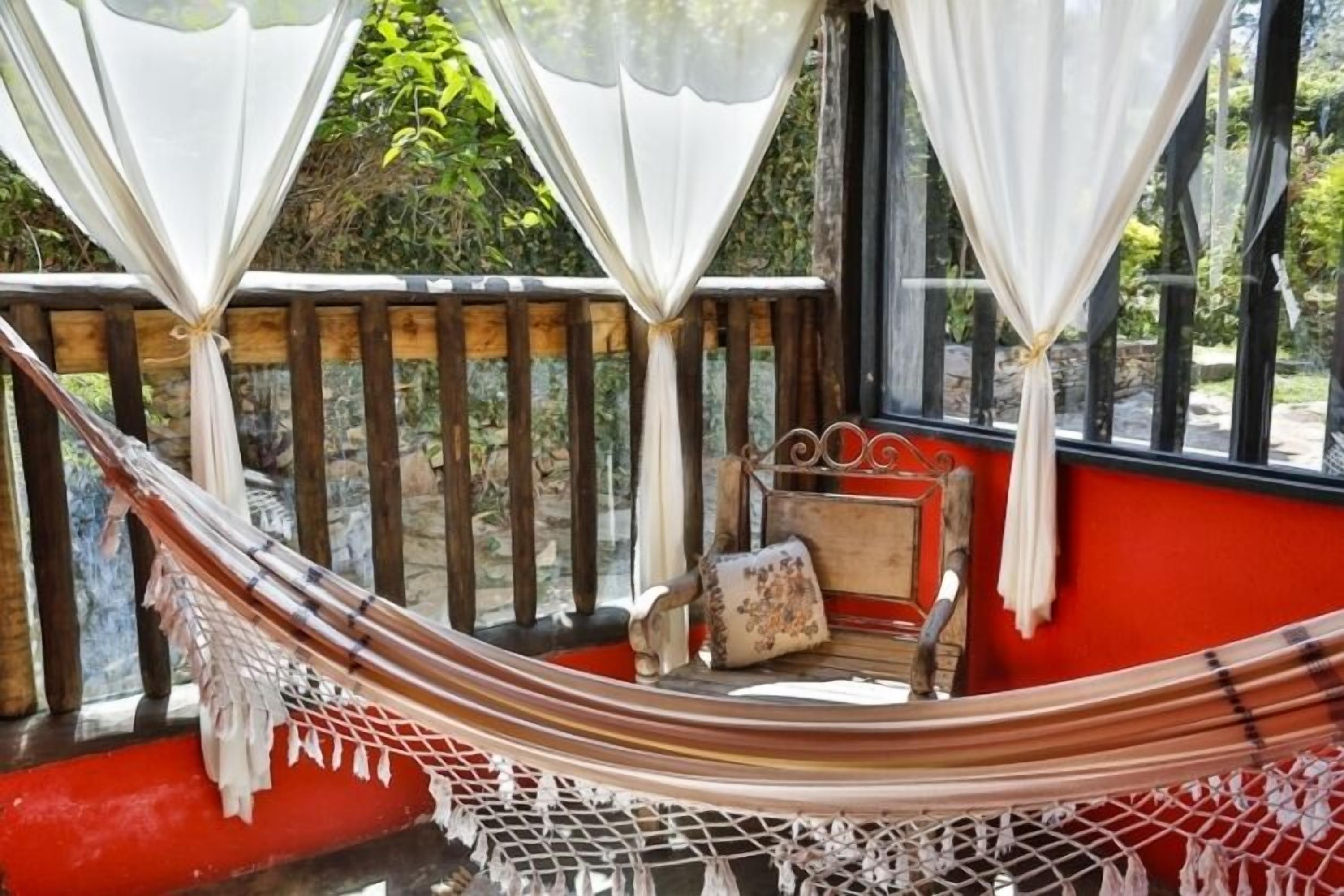 Una silla hamaca con cojín, un banco de madera y una ventana con cortinas.