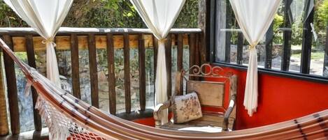 Una silla hamaca con cojín, un banco de madera y una ventana con cortinas.
