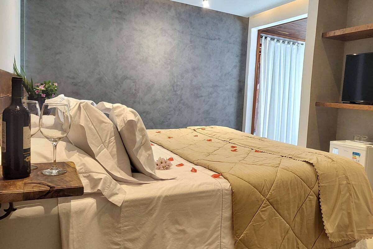 A hotel room with a bed, a TV, a minibar, and a window with curtains.