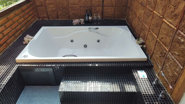 A rectangular hot tub with a white interior, surrounded by a black tiled floor and a brick wall. - Pousada Solar Dos Ipês (Santana do Riacho)