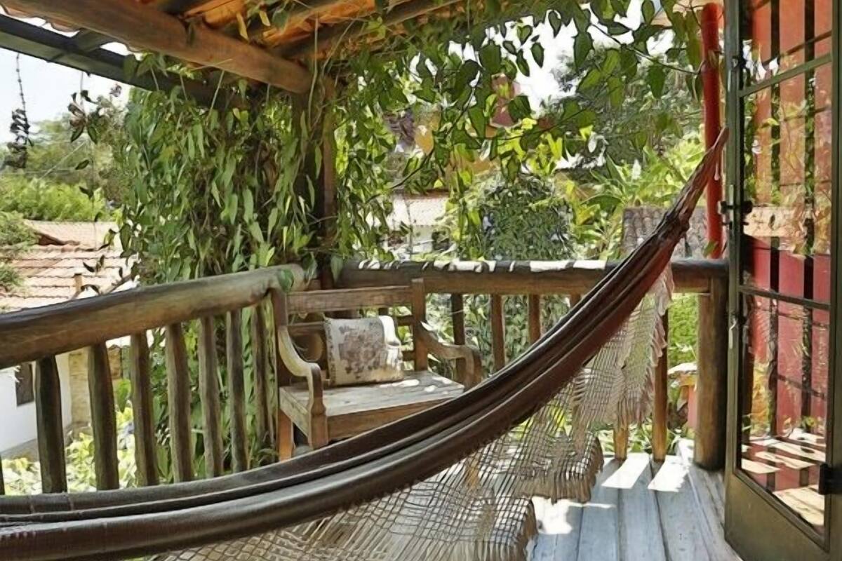 A hammock under a wooden pergola with a woven ceiling, a woven chair, and a view of greenery outside.