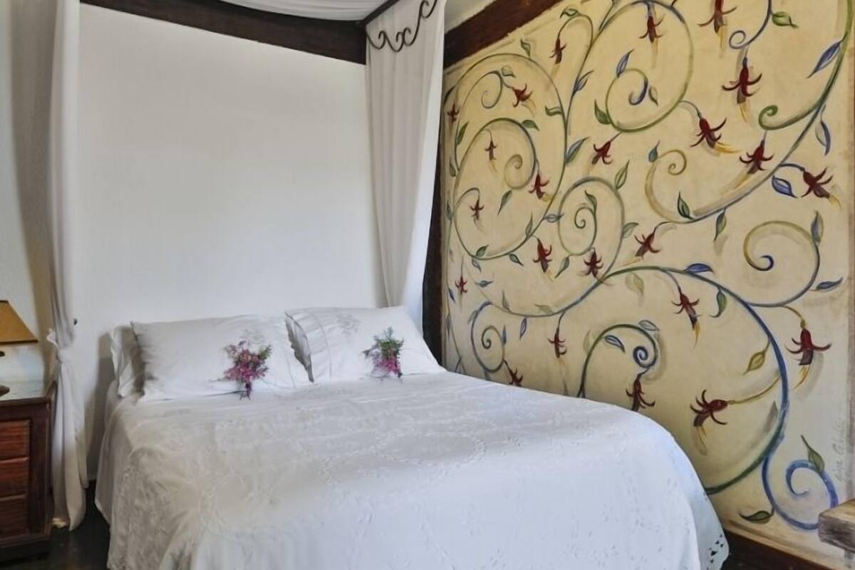 A bedroom with a bed, white curtains, and a floral-patterned headboard.