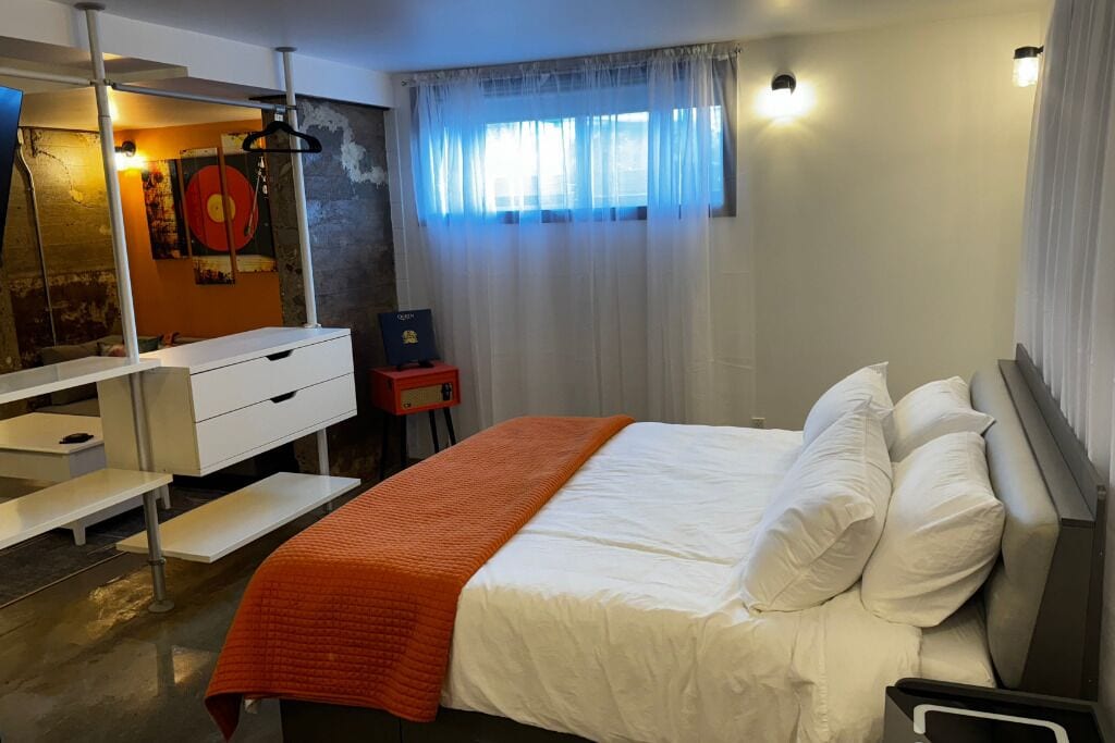 A bedroom with a bed, a desk, a chair, a mirror, and a window with curtains.