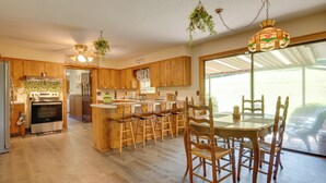 Una cocina amplia con armarios de madera, una isla central con taburetes de bar, una mesa de comedor con sillas y una lámpara colgante.