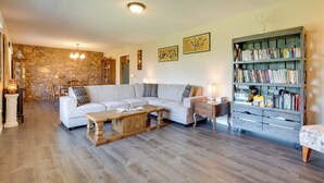 Una sala de estar con sofá blanco, mesa de centro de madera, pared de piedra, estantería y candelabro.