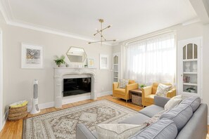 A living room with a fireplace, a sofa, a yellow armchair, and a large window with sheer curtains.