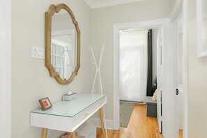 Une pièce avec un bureau en verre, un miroir à cadre en bois, une porte blanche et une vue sur une autre pièce.