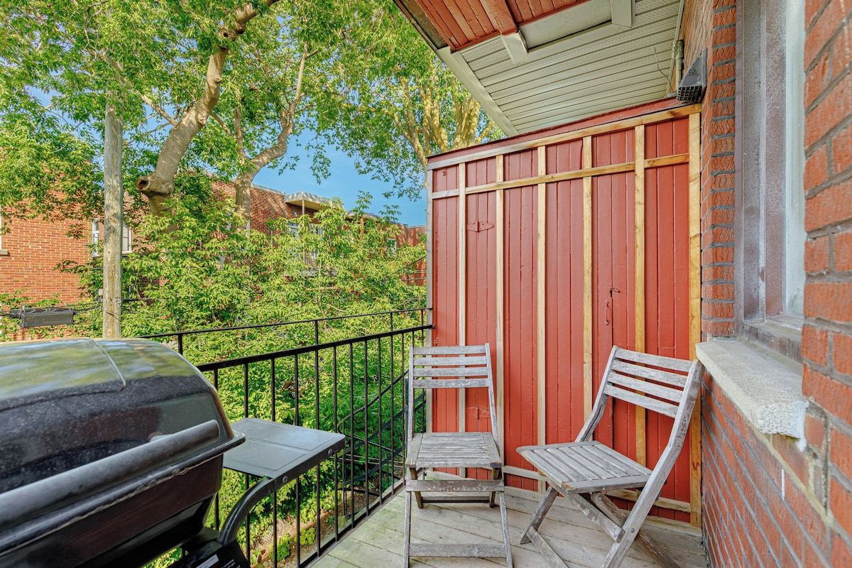 A balcony with a barbecue grill, two wooden chairs, and a red wooden wall.