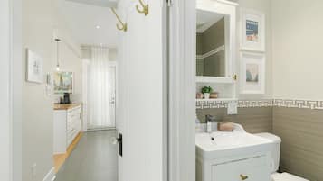 Un baño moderno con lavamanos, tocador y retrete blancos. Hay cuadros enmarcados en la pared y una planta pequeña en la encimera.