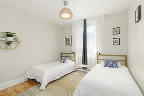 Un dormitorio con dos camas individuales, una mesita de noche, una lámpara colgante y un estante en la pared con plantas.