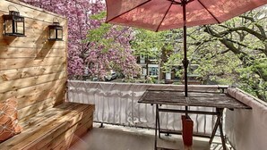 Una terraza de madera con una mesa y un banco, rodeada de cerezos en flor y una valla blanca.