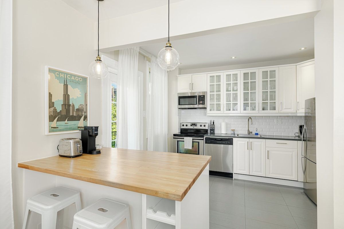 A modern kitchen with white cabinets, a wooden island, and stainless steel appliances.