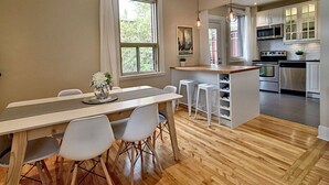 Una cocina moderna con armarios blancos, una isla central y un comedor con mesa de madera y sillas blancas.