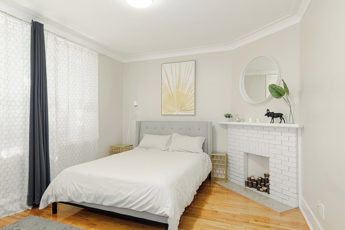 Un dormitorio con cama, chimenea, espejo y ventana con cortinas.