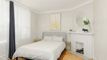 Un dormitorio con cama, chimenea, espejo y ventana con cortinas.