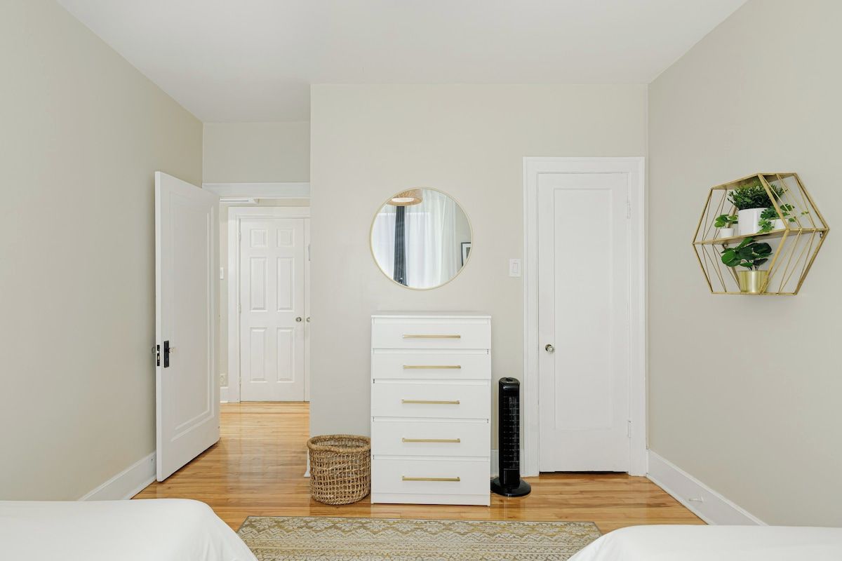 A bedroom with a bed, a dresser, a mirror, a heater, and a wall-mounted plant shelf.