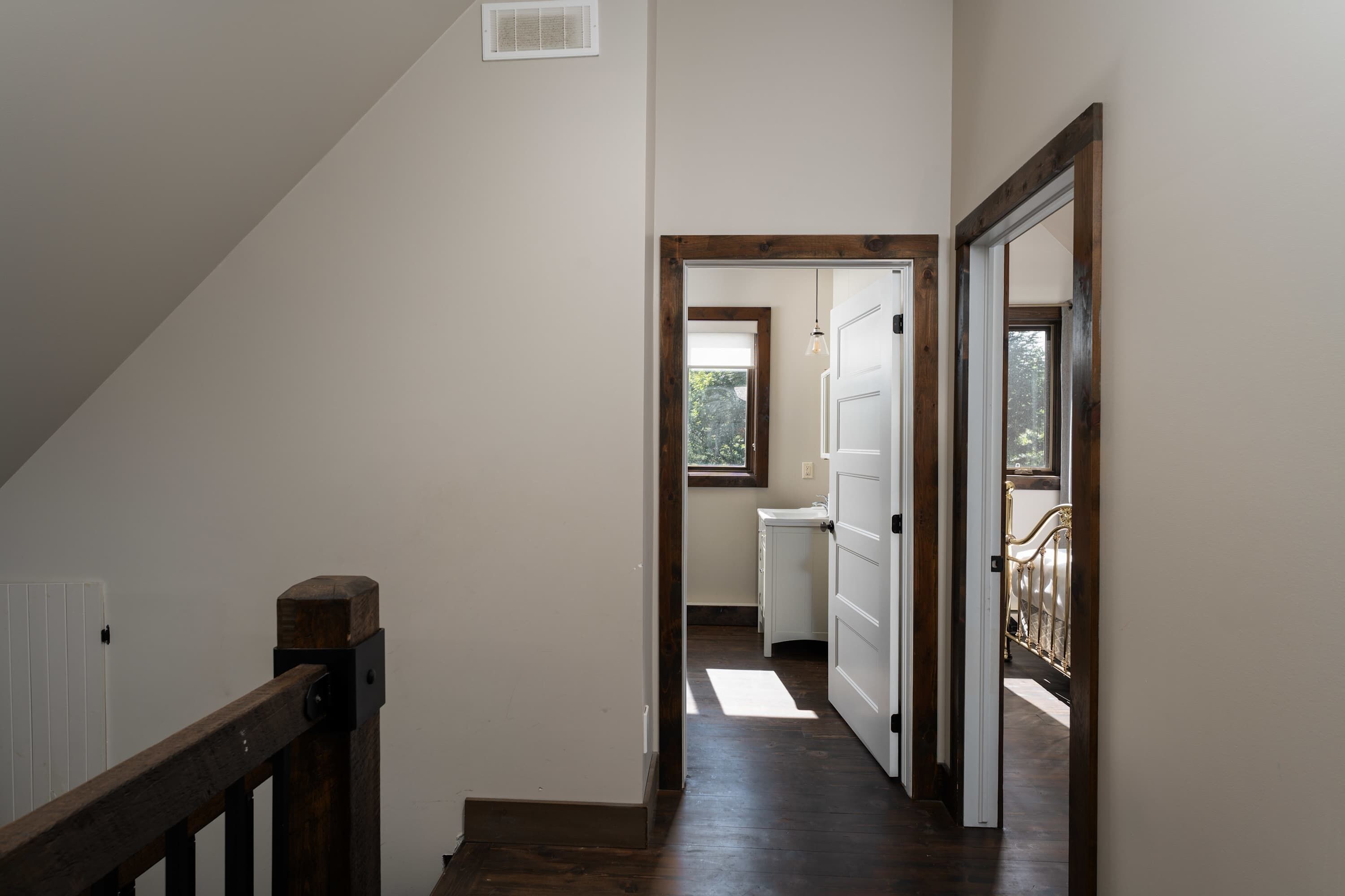 A narrow hallway with wooden flooring, a white door at the end, and a window allowing natural light.