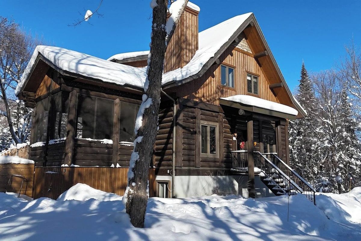 A log cabin with a steeply pitched roof, a front porch, and a staircase leading to the entrance.