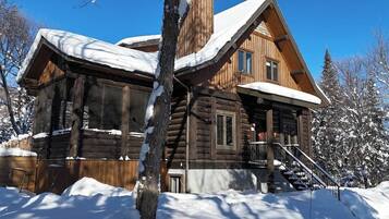 A log cabin with a steeply pitched roof, a front porch, and a staircase leading to the entrance.