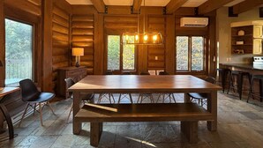 L'intérieur d'un chalet en bois comprend une grande table à manger, des chaises, un banc, un lustre et un coin cuisine.