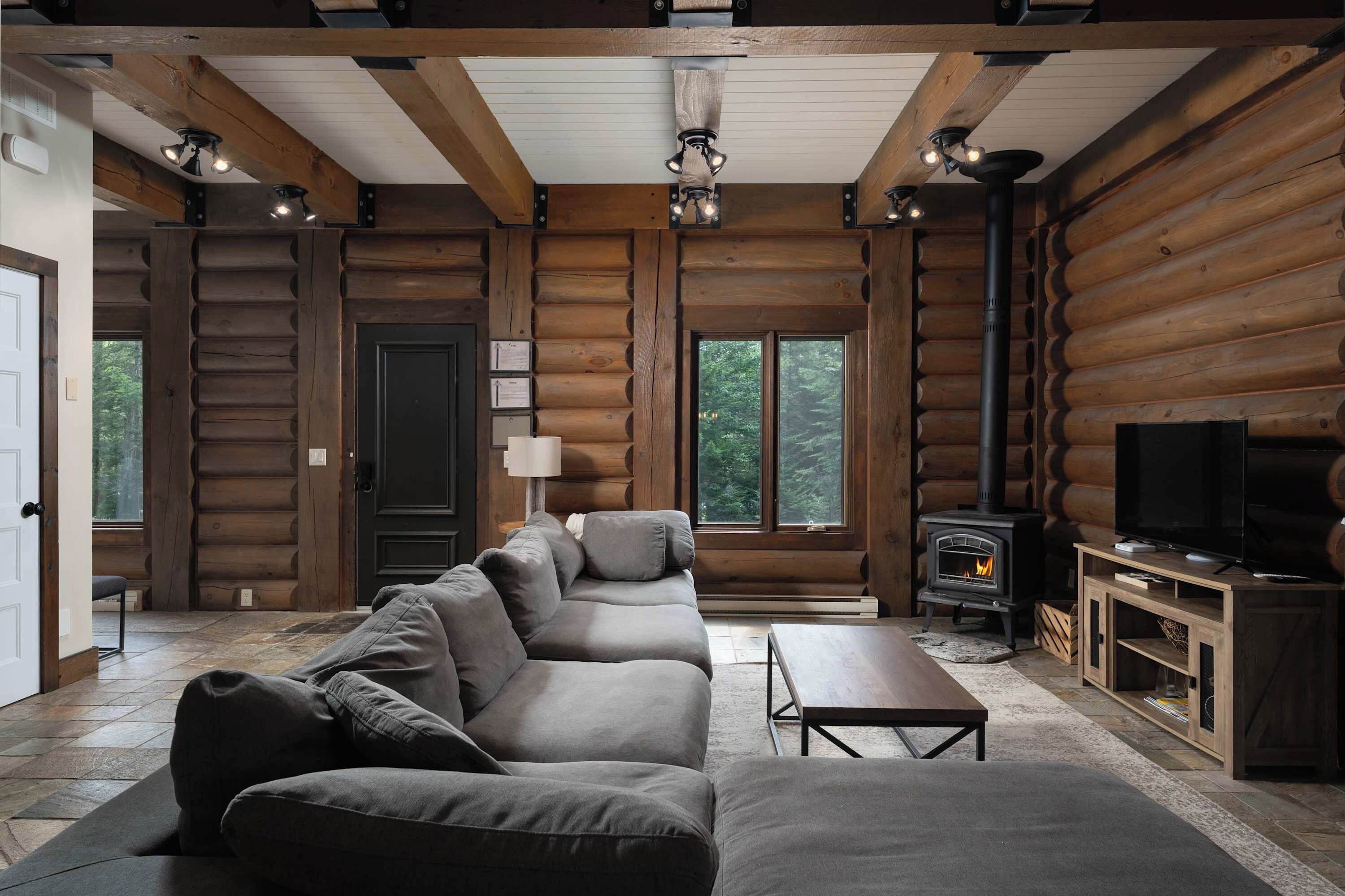 A log cabin interior with a sofa set, a television, and a wood-burning stove.