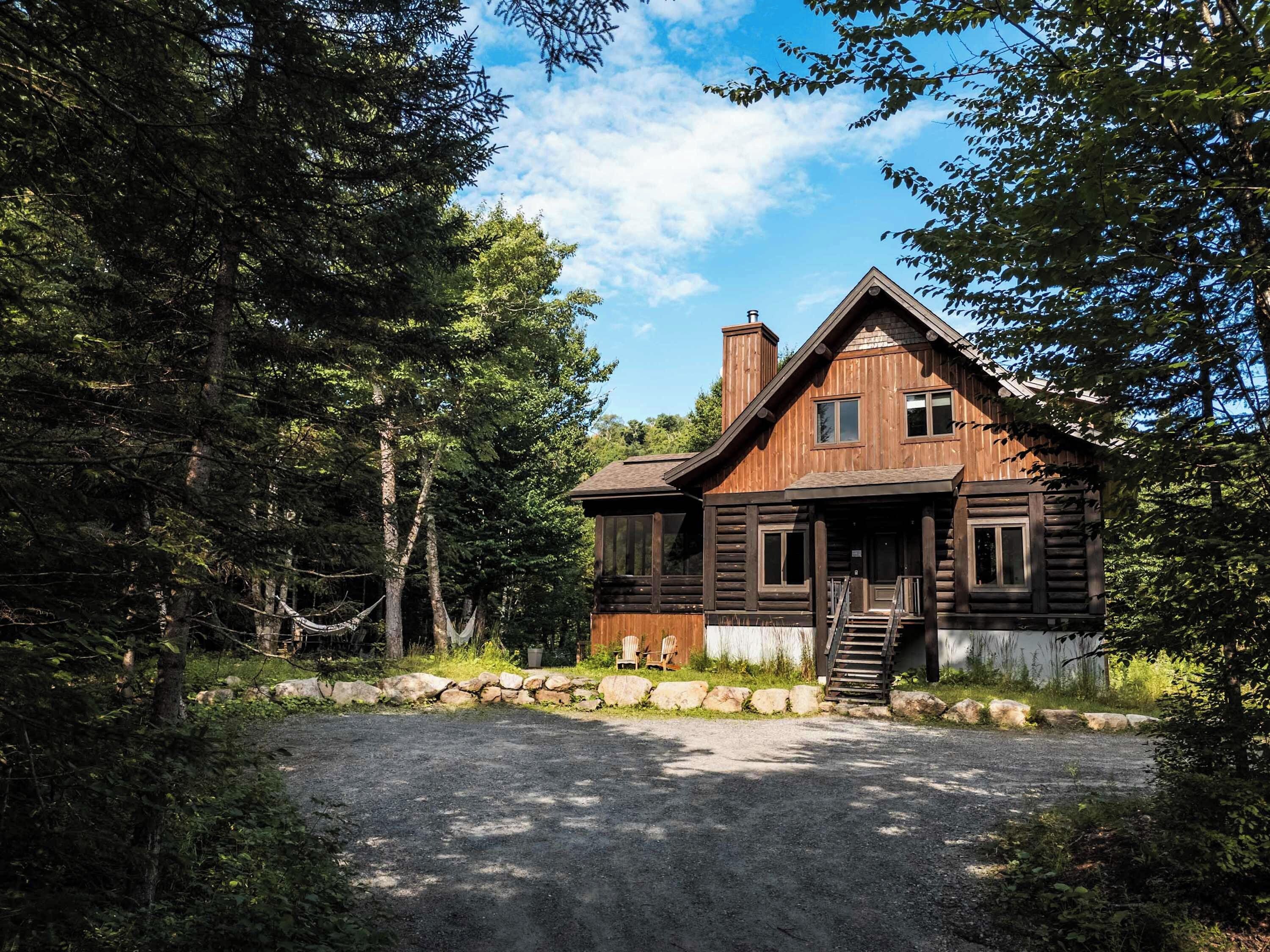 A rustic log cabin with a stone foundation, a wooden porch, and a chimney.
