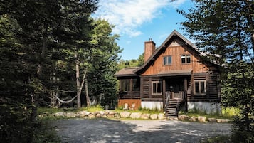 A rustic log cabin with a stone foundation, a wooden porch, and a chimney.