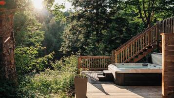 Une terrasse en bois avec un jacuzzi, entourée d’une végétation luxuriante et d’arbres.