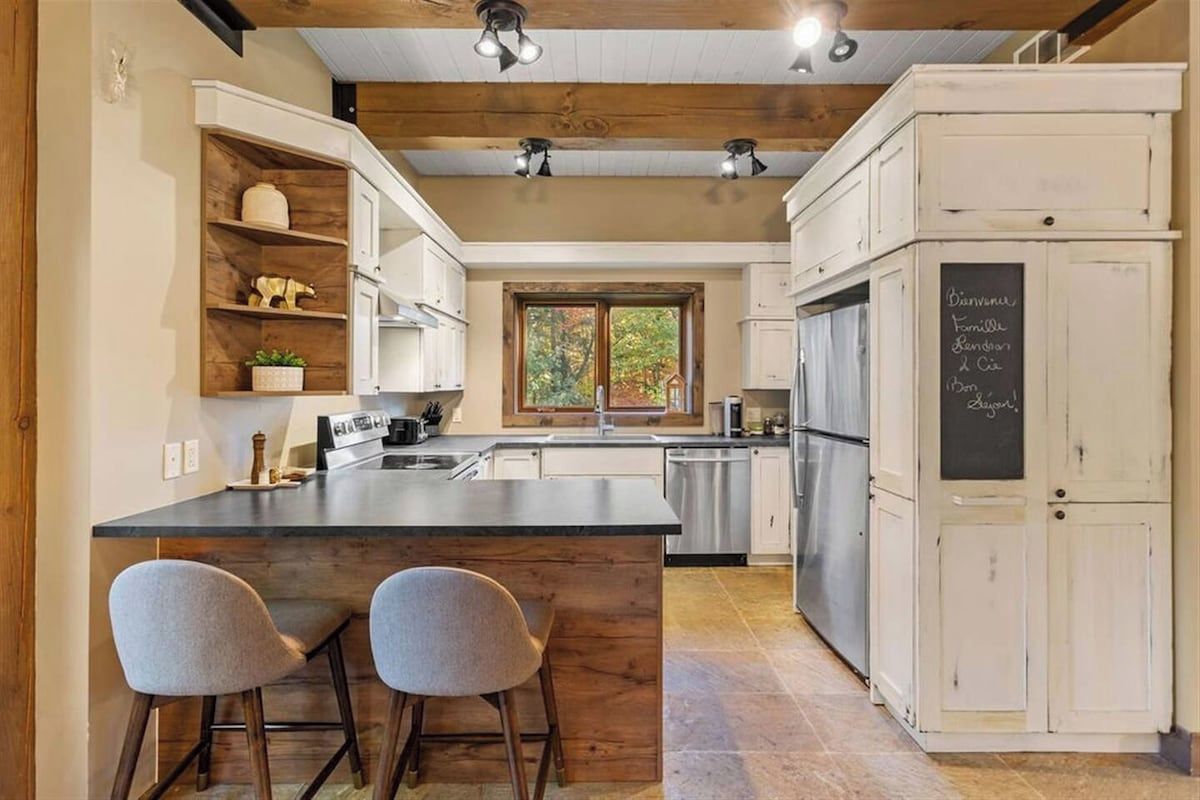 A kitchen with a central island, bar stools, white cabinetry, and a chalkboard with menu items.