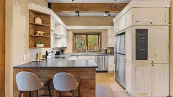 A kitchen with a central island, bar stools, white cabinetry, and a chalkboard with menu items.