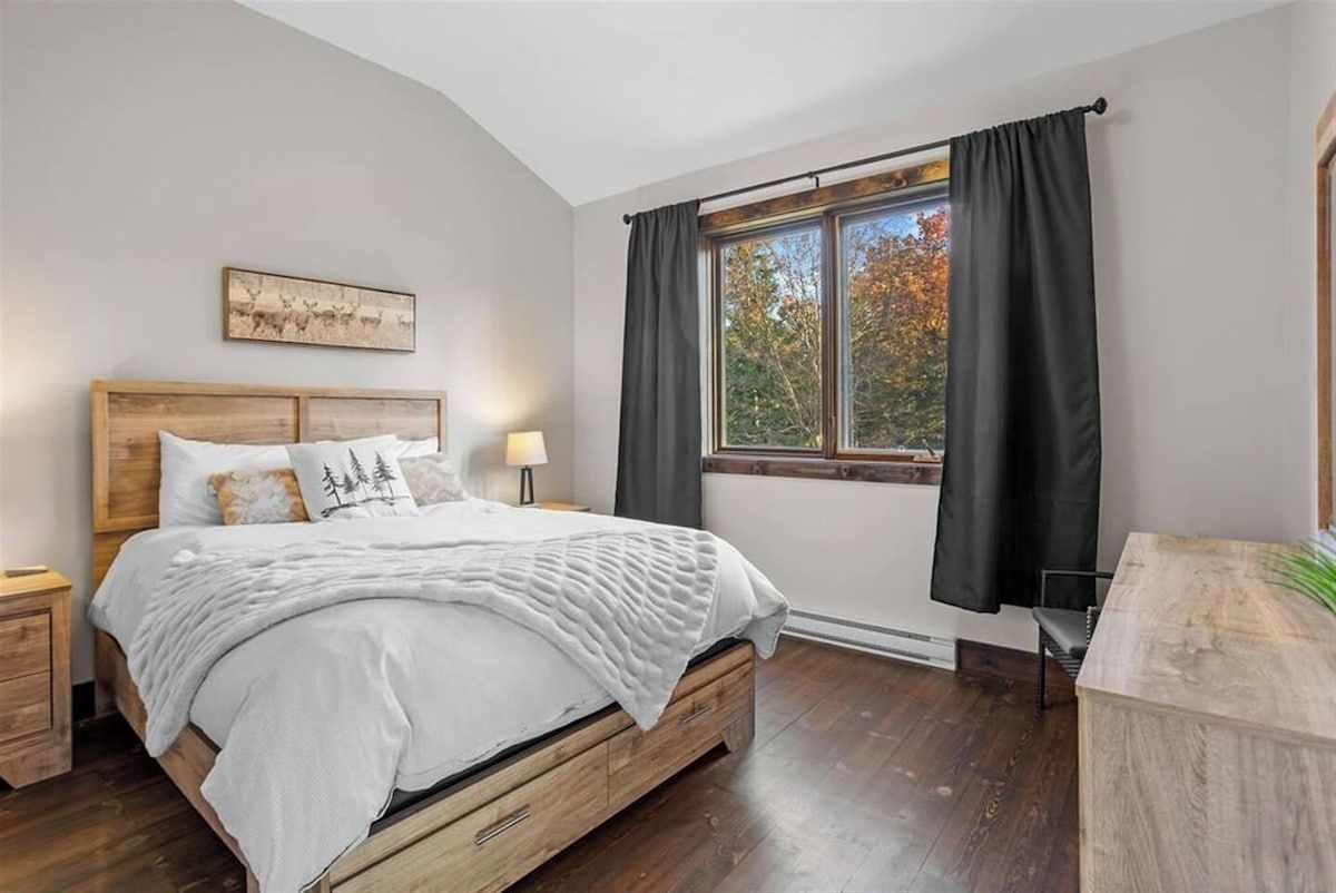 Ein Schlafzimmer mit Bett, Nachttisch, einem Fenster mit Vorhängen und einem Bild an der Wand.