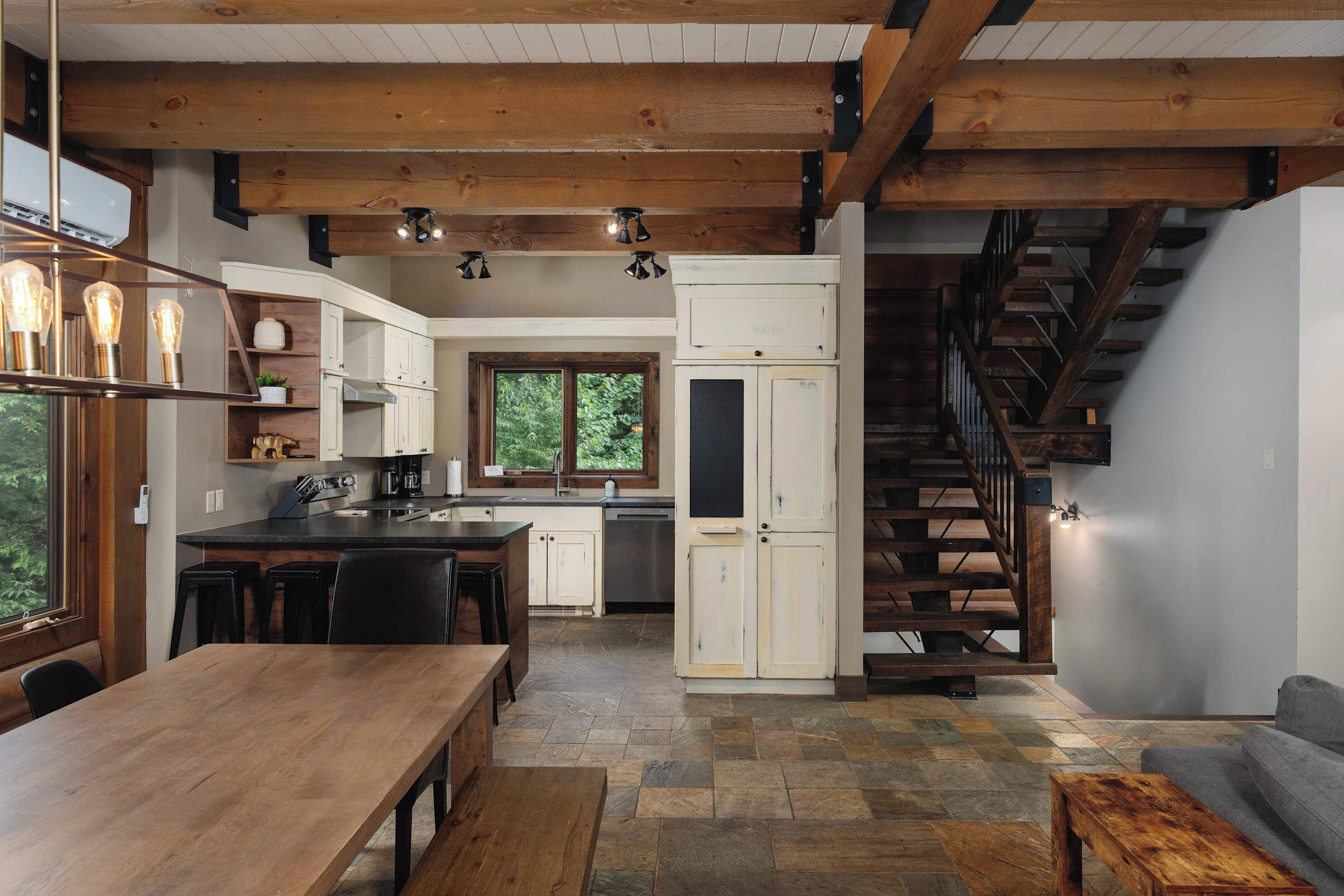 A modern kitchen with a central island, wooden beams, and a stone-tiled floor.