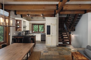 A modern kitchen with a central island, wooden beams, and a stone-tiled floor.