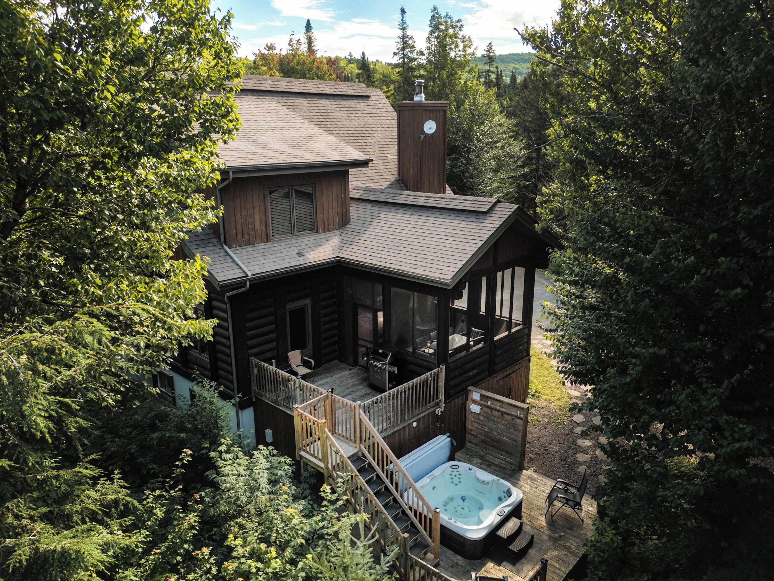 A cabin with a hot tub, deck, and a view of the surrounding forest.