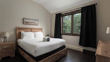 Un dormitorio con una cama de madera, una mesita de noche, una lámpara en la mesita, una ventana con cortinas y un cuadro en la pared.