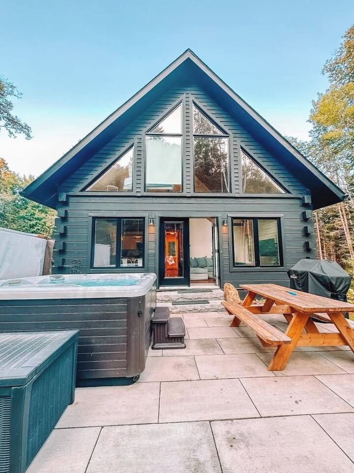 A modern two-story house with a large deck, a hot tub, and a picnic table.