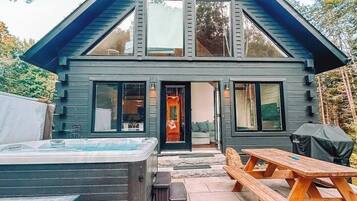 A modern two-story house with a large deck, a hot tub, and a picnic table.