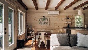 L’intérieur chaleureux d’un chalet avec un plafond en bois, un coin repas comprenant une table et des chaises, un canapé et un coin cuisine avec un évier et des étagères.