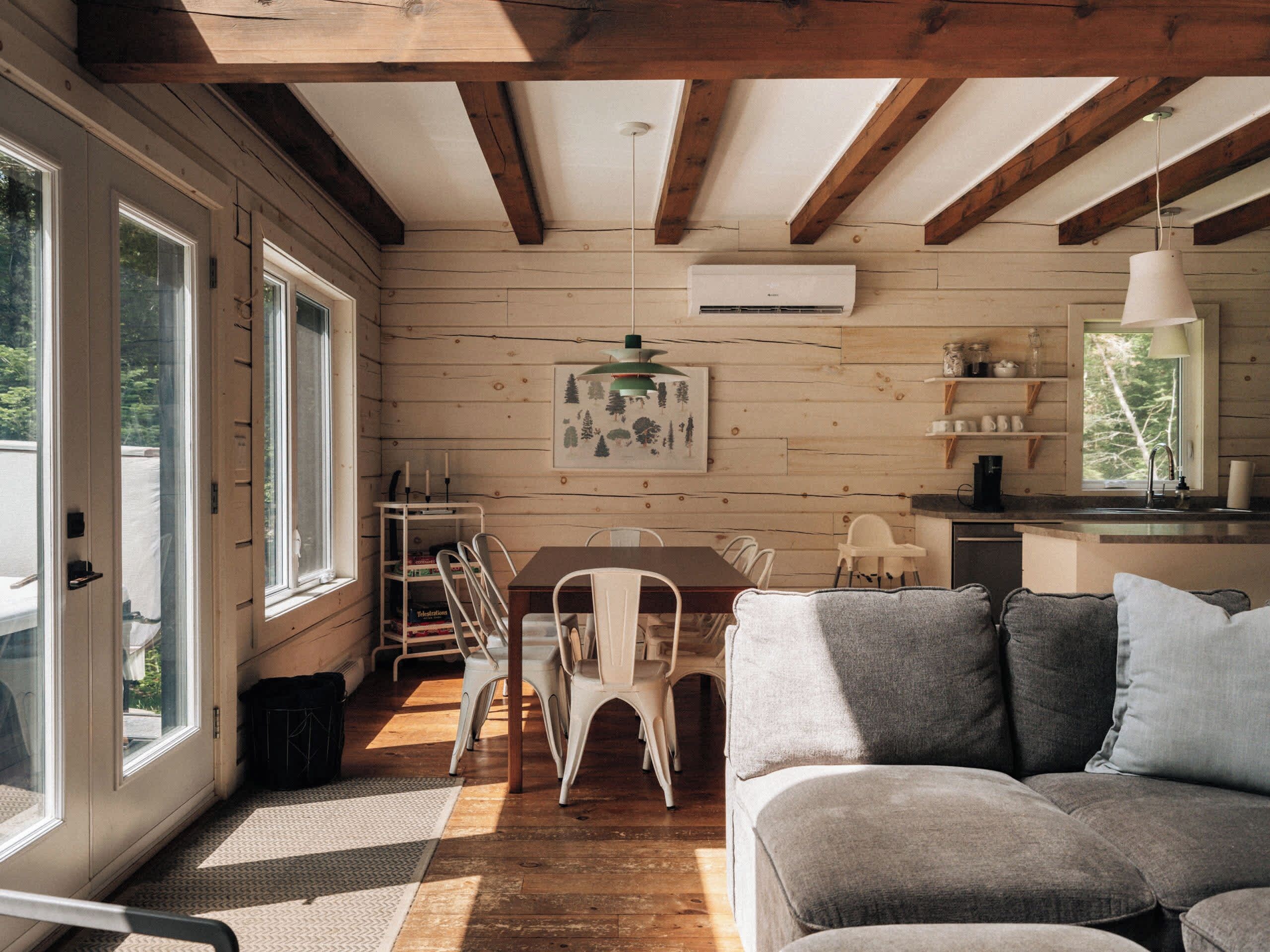 Interior acogedor de una cabaña con detalles de madera, un comedor con mesa y sillas, un sofá y una cocina con fregadero y estanterías.