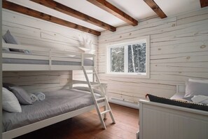 A bunk bed room with a ladder, a window with a view of trees, and a radiator.