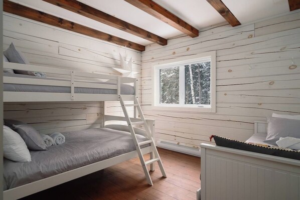 A bunk bed room with a ladder, a window with a view of trees, and a radiator.