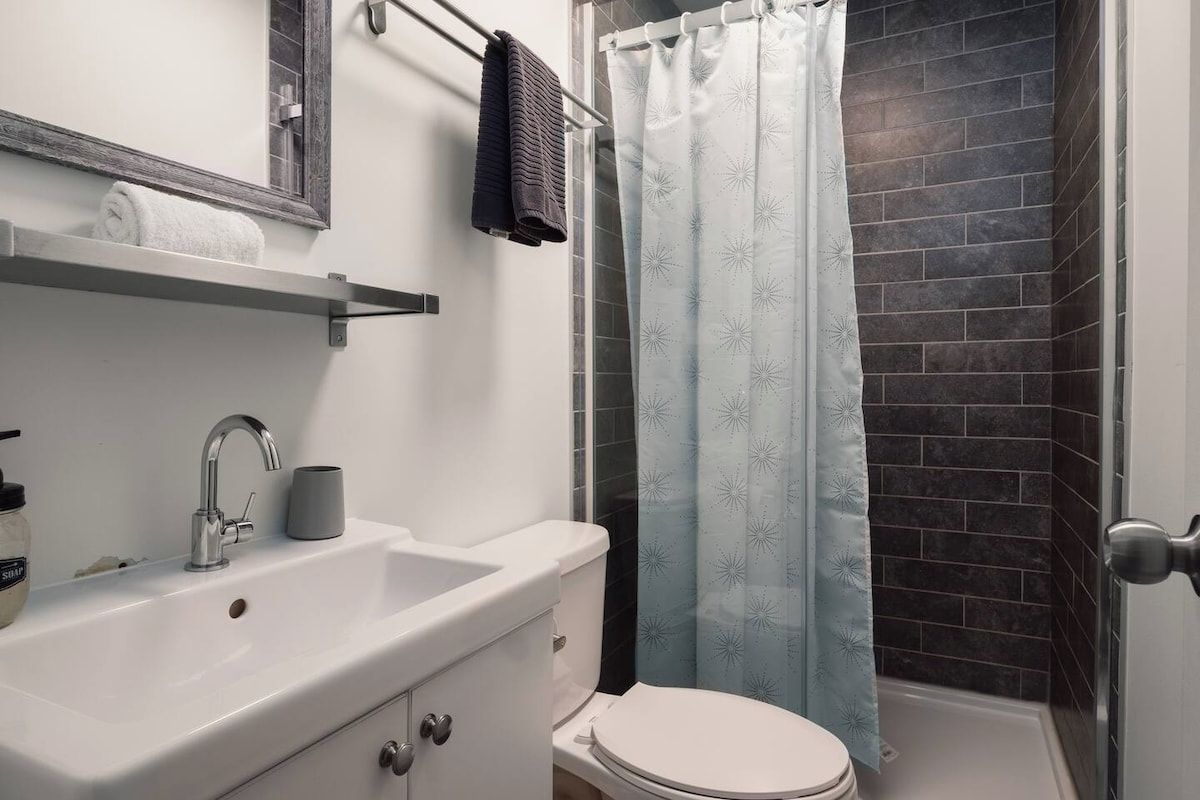 Ein Badezimmer mit weißem Waschbecken, Toilette und Dusche mit gemustertem Vorhang.