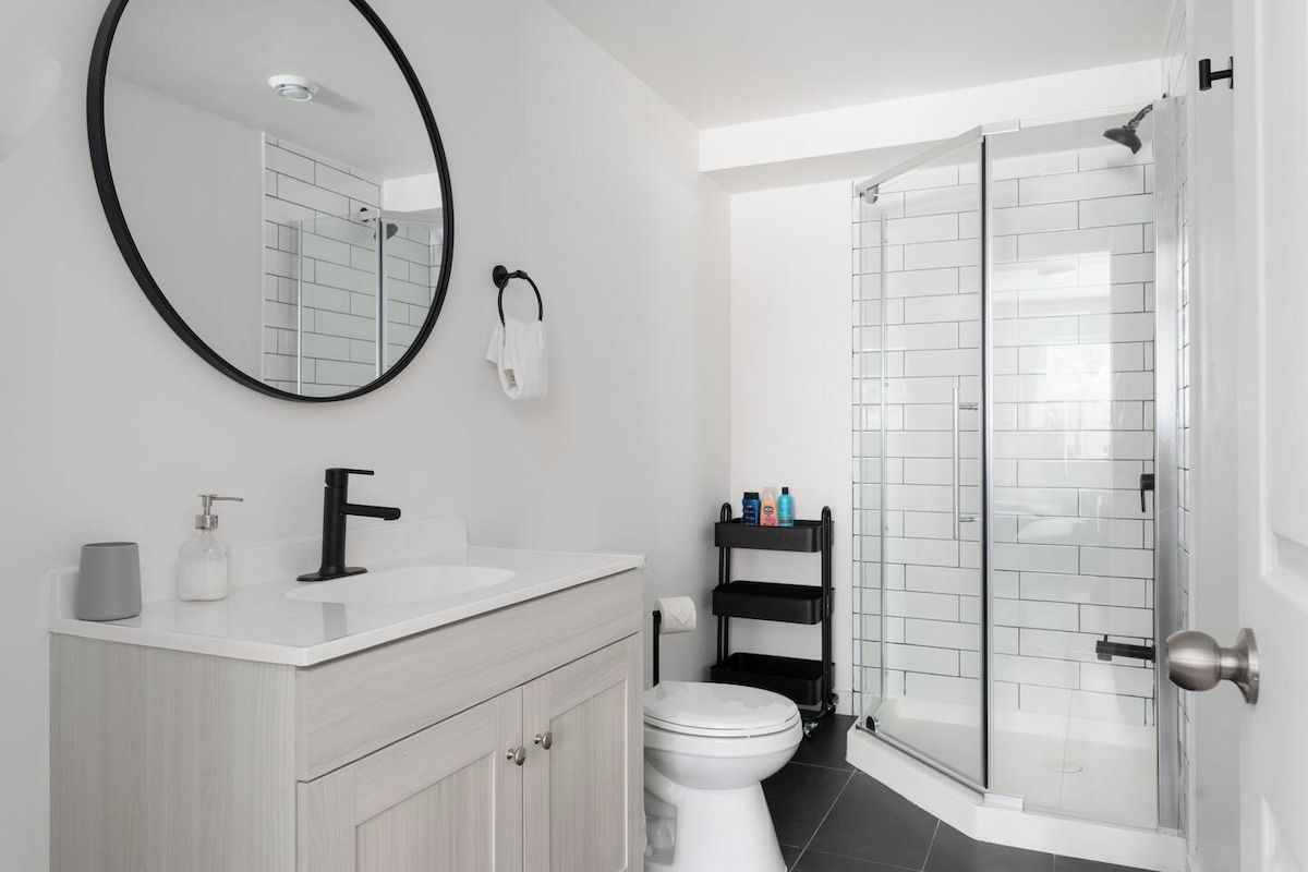 A modern bathroom with a white sink, black faucet, and a round mirror.