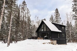 A cabin with a steep roof, large windows, and a snow-covered ground.