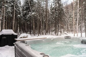 Un jacuzzi rodeado de árboles cubiertos de nieve en un entorno boscoso.