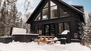 Une cabane dotée de grandes fenêtres, d’une terrasse en bois et d’une table de pique-nique.