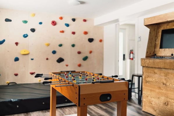 A foosball table in a room with a climbing wall and a wooden cabinet.