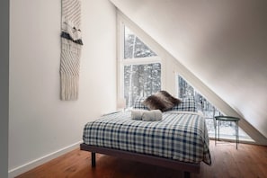 A bedroom with a bed, a window, and a view of a snowy forest.